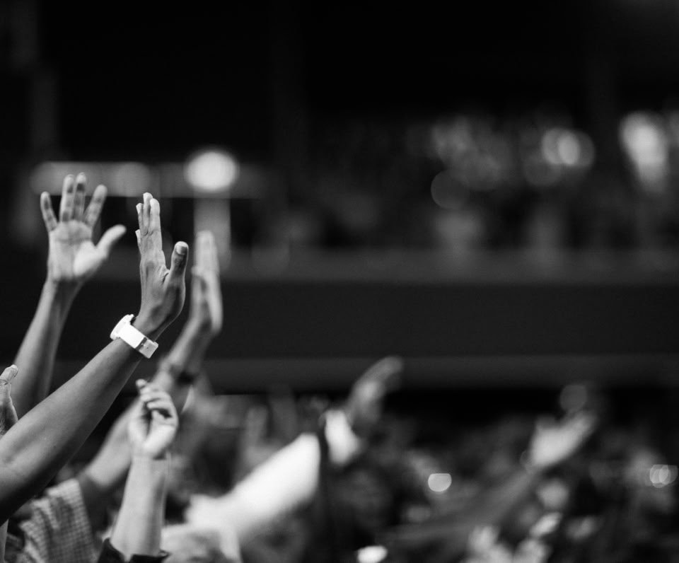 Black and white image of audience with hands raised, capturing concert energy.