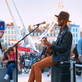 Talented street performer playing acoustic guitar outdoors in a bustling city square during the day.